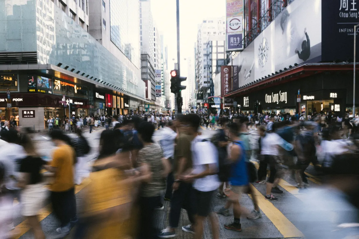 A crowded city shopping street lined with illuminated storefront signage and blurred, hurrying pedestrians.